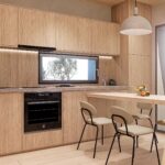 Moderne, minimalistische Küche mit Holzverkleidung, integrierten Geräten und großzügigem Esstisch.
